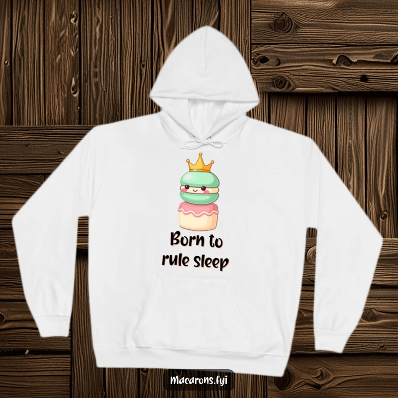 Funny macaron character wearing a small crown, looking regal atop a tiny cake, featured on a warm hoodie.