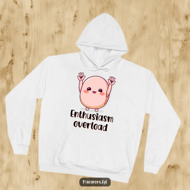 Funny macaron character joyfully cheering with tiny hands raised high, depicted on a cozy hoodie for warm celebration.